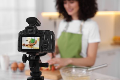 Photo of Food blogger cooking while recording video in kitchen, focus on camera