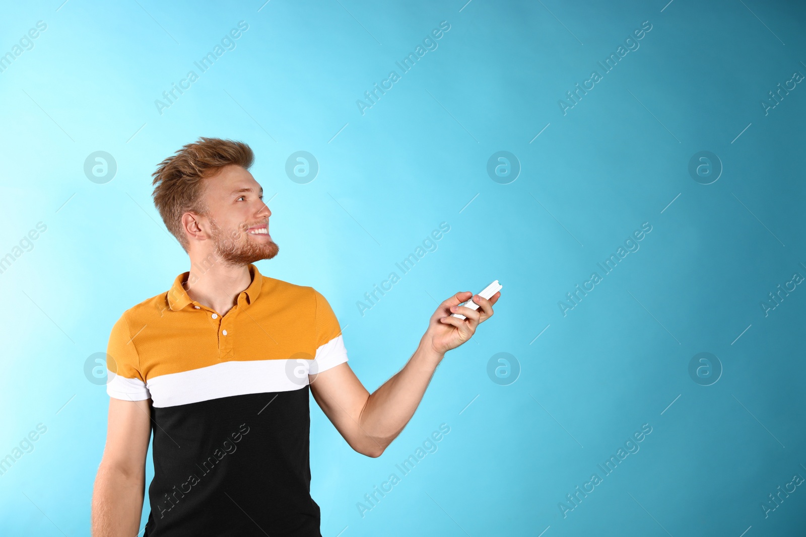 Photo of Young man with air conditioner remote on blue background. Space for text