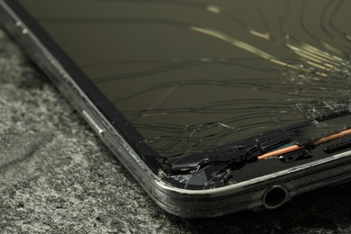 Photo of Smartphone with cracked screen on grey stone background, closeup. Device repair