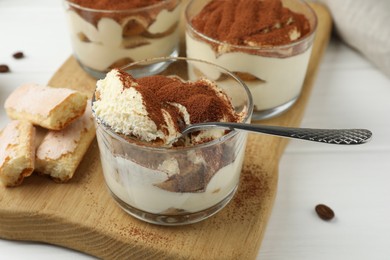 Photo of Delicious tiramisu in glasses, cookies and spoon on white table, closeup