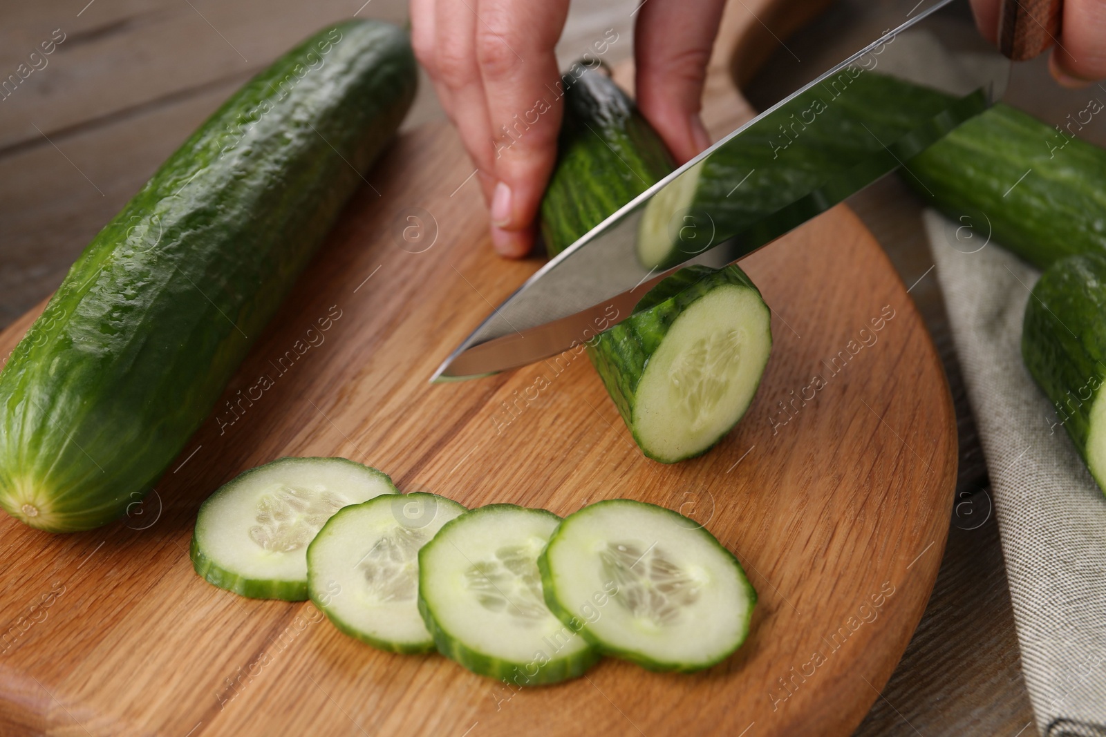 Photo of Woman cutting cucumber on wooden board at table, closeup