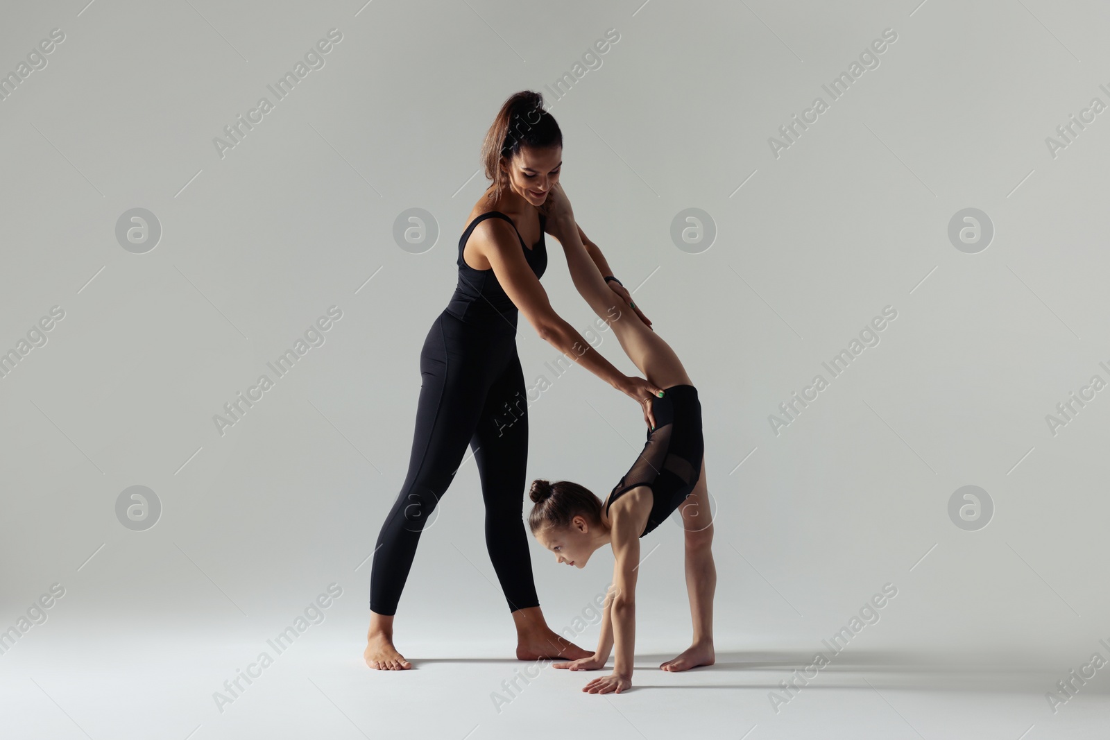 Photo of Gymnastic coach helping little girl to do split on white background