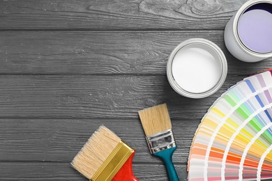 Flat lay composition with cans of paint, brushes and palette on grey wooden background. Space for text