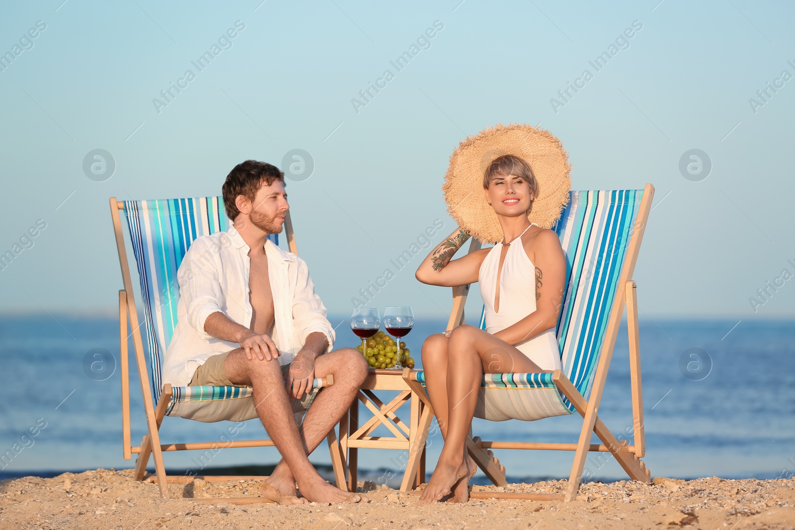 Photo of Young couple having picnic with wine and grapes on beach