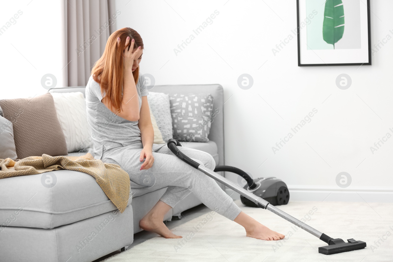 Photo of Tired housewife sitting on sofa instead of hoovering at home