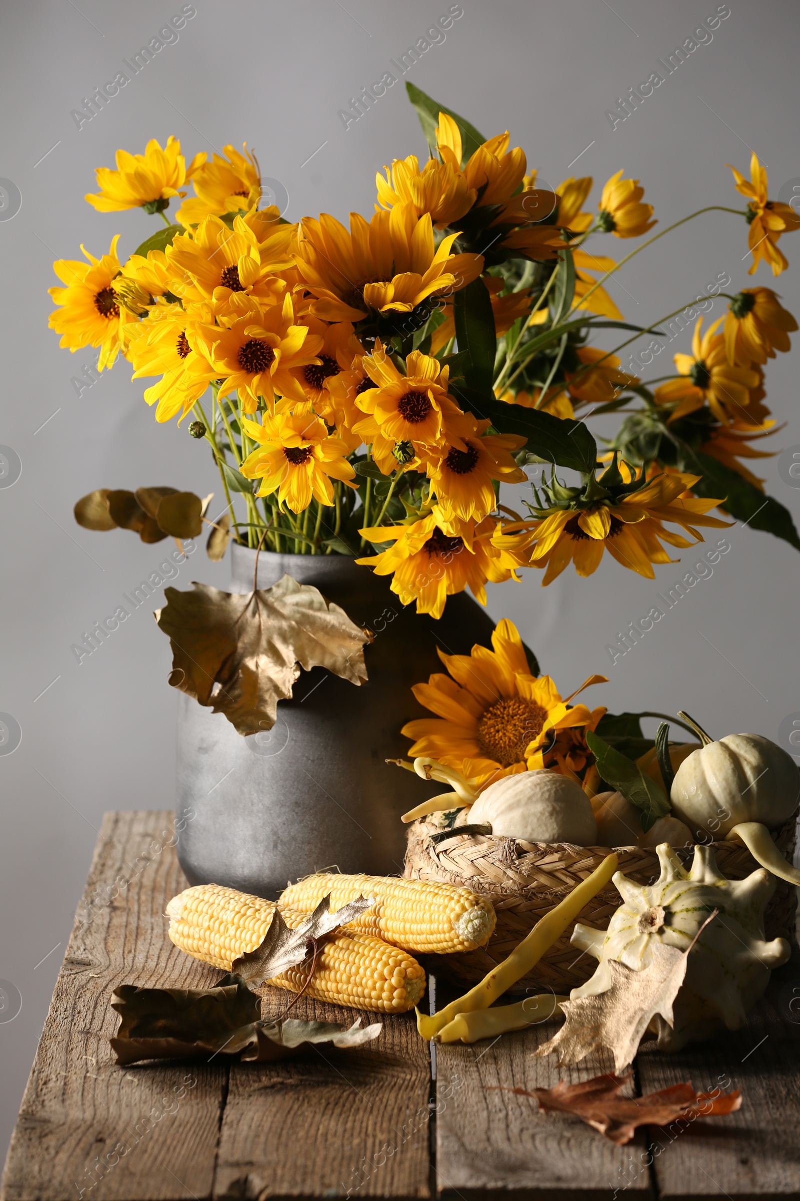 Photo of Beautiful autumn bouquet, small pumpkins and corn cobs on wooden table against grey background