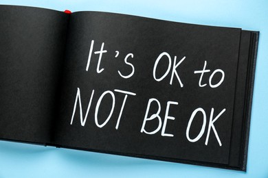 Photo of Notebook with phrase It`s Ok To Not Be Ok on light blue background, top view