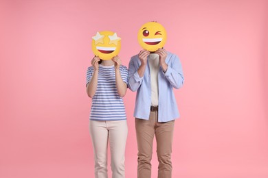 People covering faces with emoticons on pink background