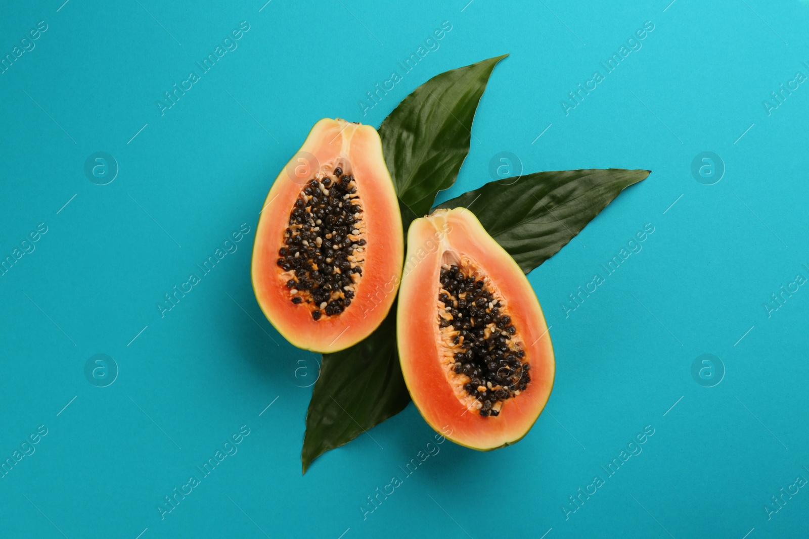 Photo of Fresh halved papaya fruit with green leaves on blue background, flat lay