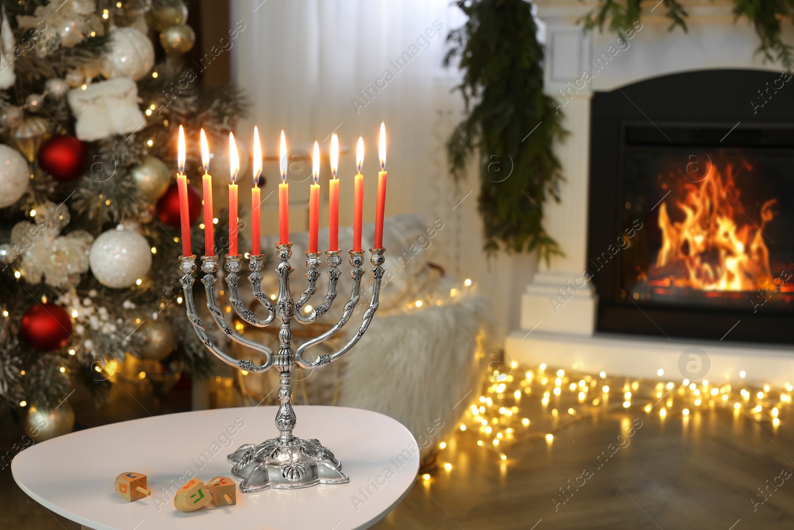 Photo of Silver menorah near dreidels with symbols Nun, Gimel, He, Pe against fireplace, space for text