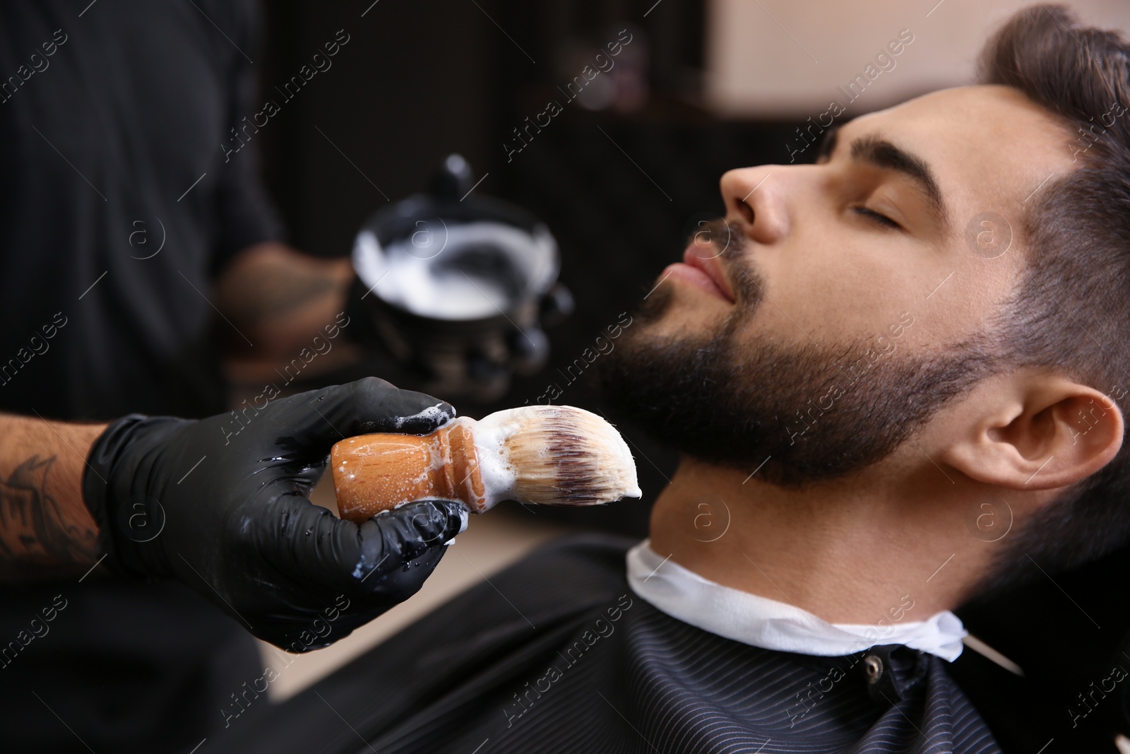 Photo of Professional hairdresser applying shaving foam onto client's skin in barbershop