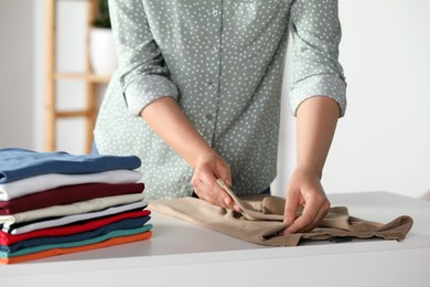 Photo of Woman folding clothes at white table indoors, closeup