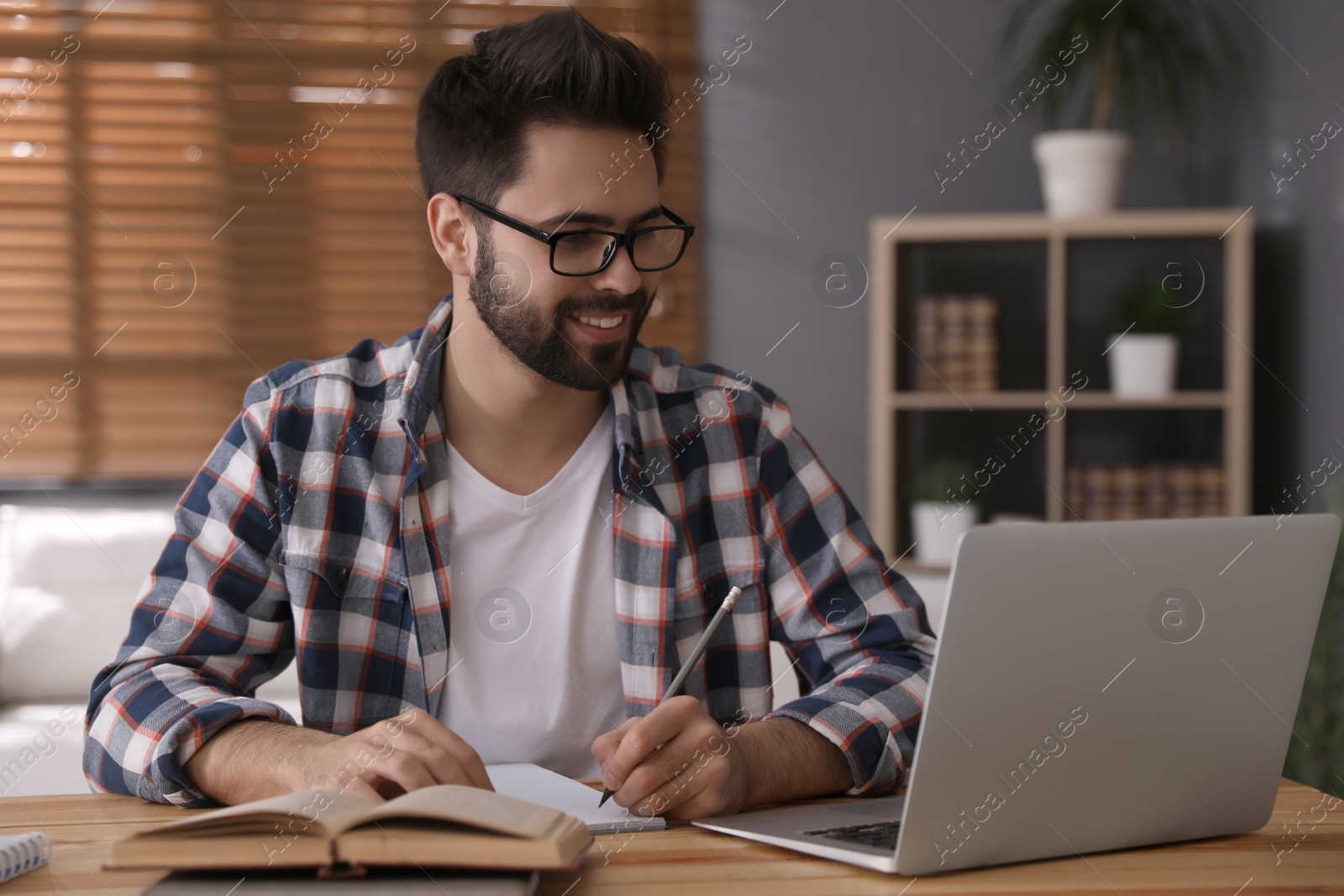 Photo of Young man watching webinar at table in room