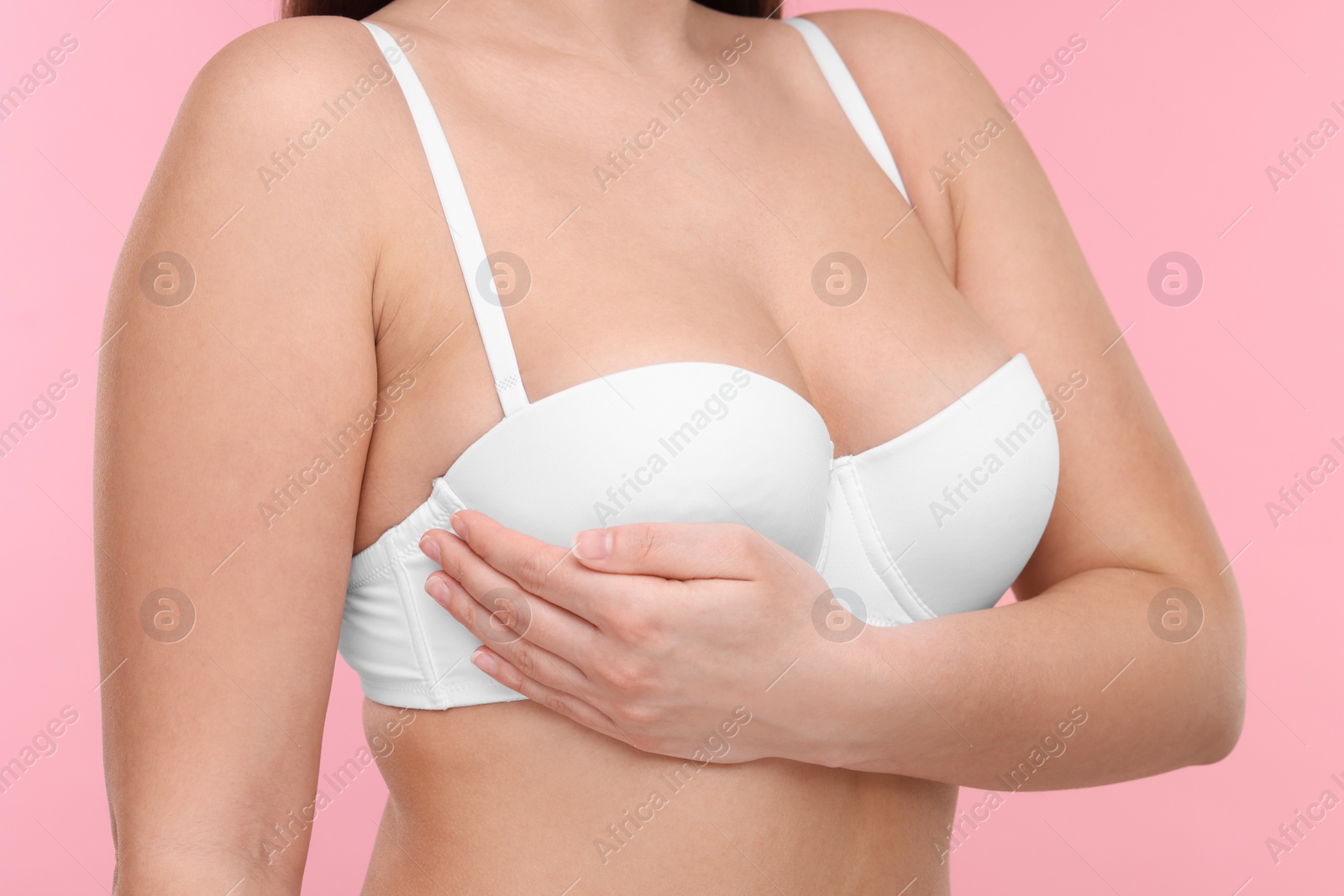 Photo of Mammology. Woman in bra doing breast self-examination on pink background, closeup