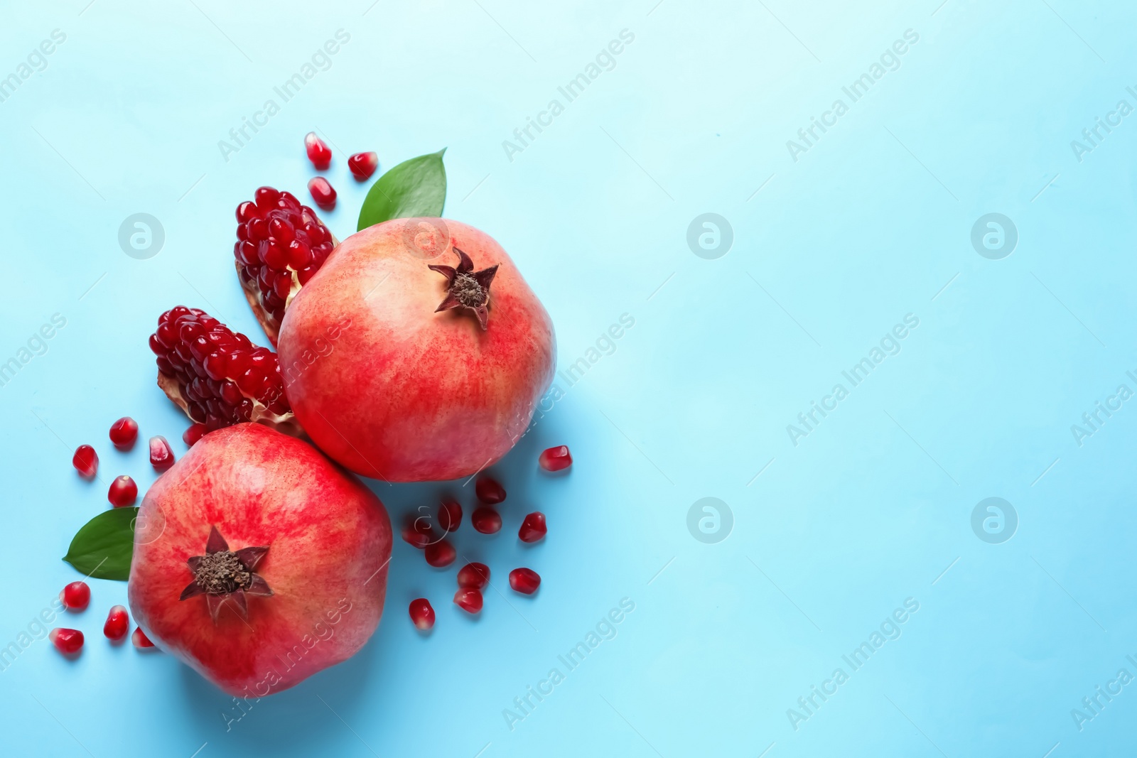 Photo of Ripe pomegranates and leaves on color background, top view with space for text