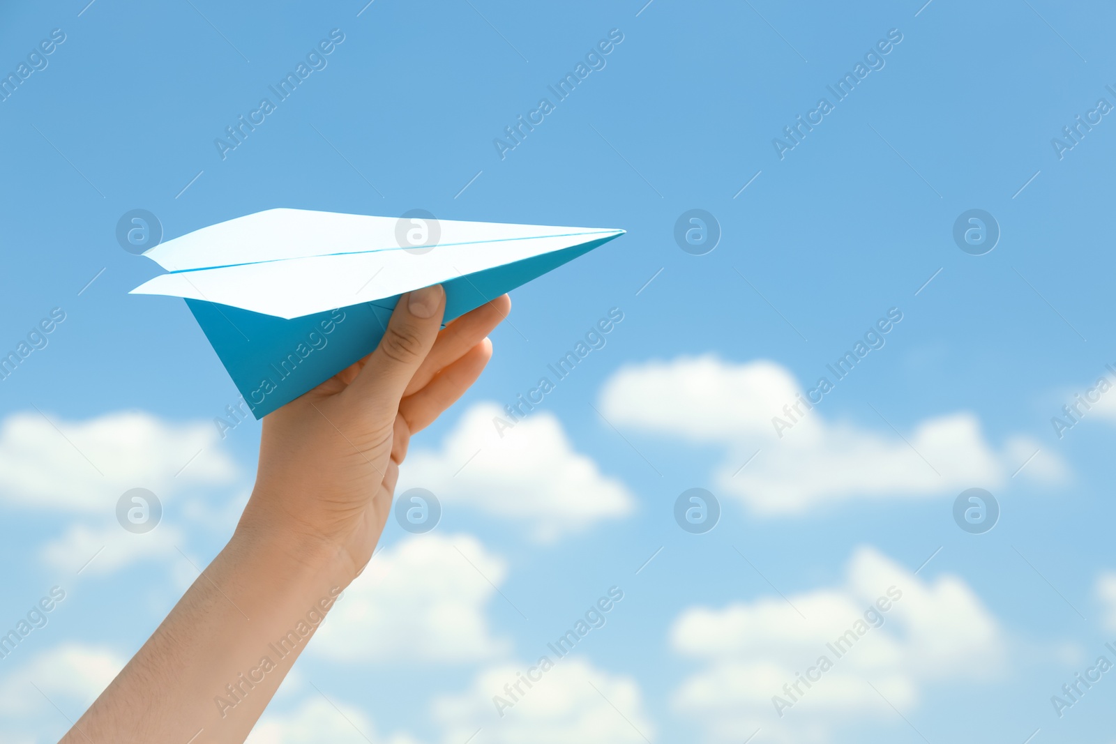 Photo of Woman holding paper plane against blue sky, closeup. Space for text