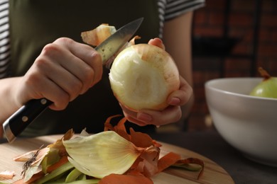 Woman peeling fresh onion at table indoors, closeup