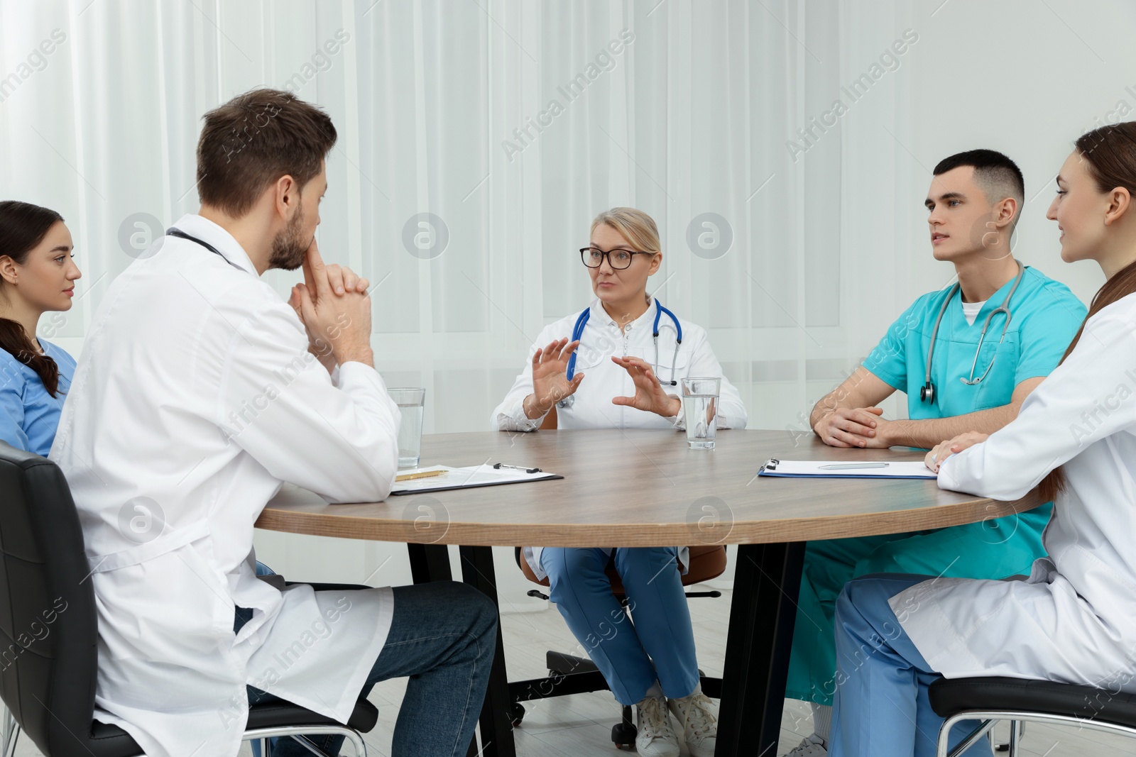 Photo of Medical conference. Team of doctors having discussion at wooden table in clinic