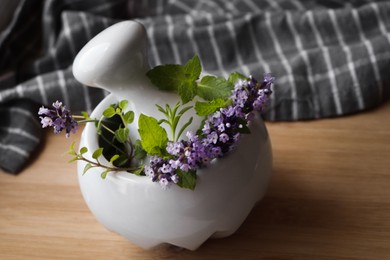 Photo of Mortar with fresh lavender flowers, herbs and pestle on wooden table, closeup