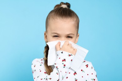 Photo of Sick girl blowing nose in tissue on turquoise background. Cold symptoms