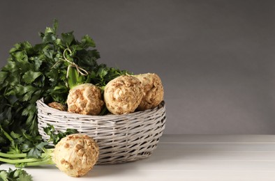 Fresh raw celery roots in wicker basket on white wooden table. Space for text