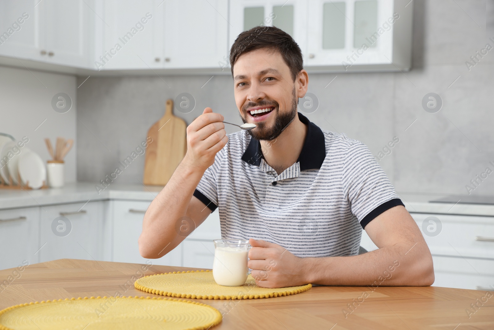 Photo of Handsome man eating tasty yogurt at table in kitchen