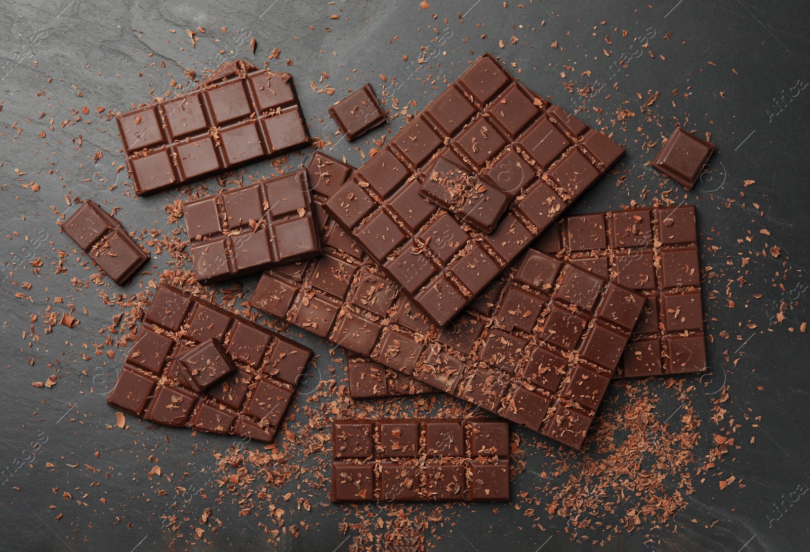 Photo of Pieces and shavings of tasty chocolate bars on grey table, flat lay