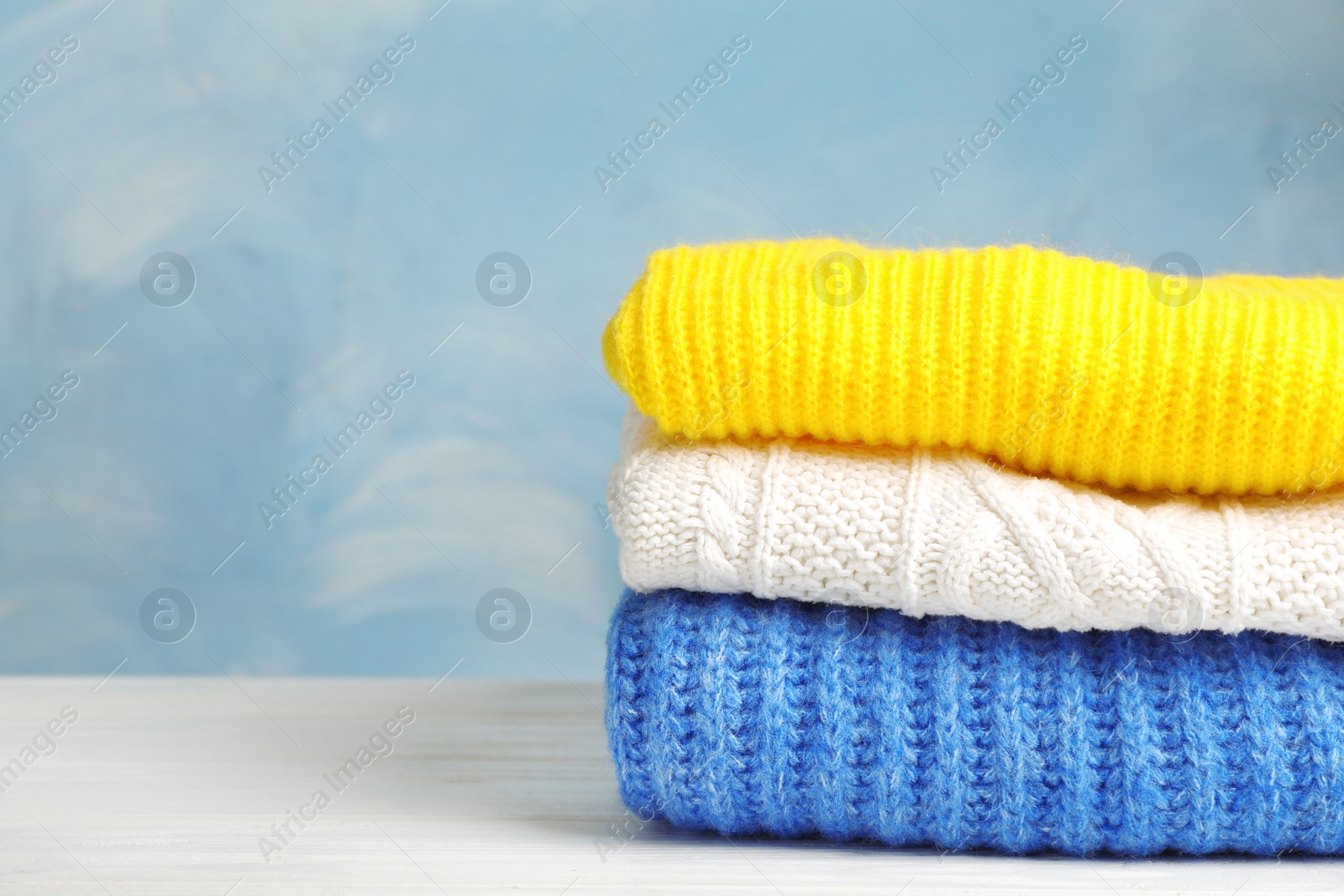 Photo of Stack of folded knitted sweaters on table. Space for text