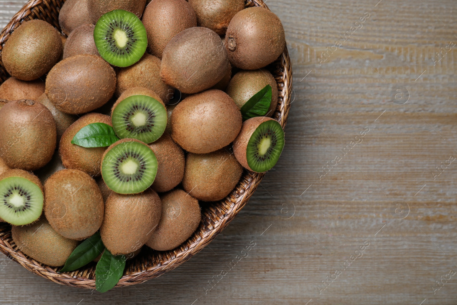 Photo of Fresh ripe kiwis in wicker bowl on wooden table, top view. Space for text