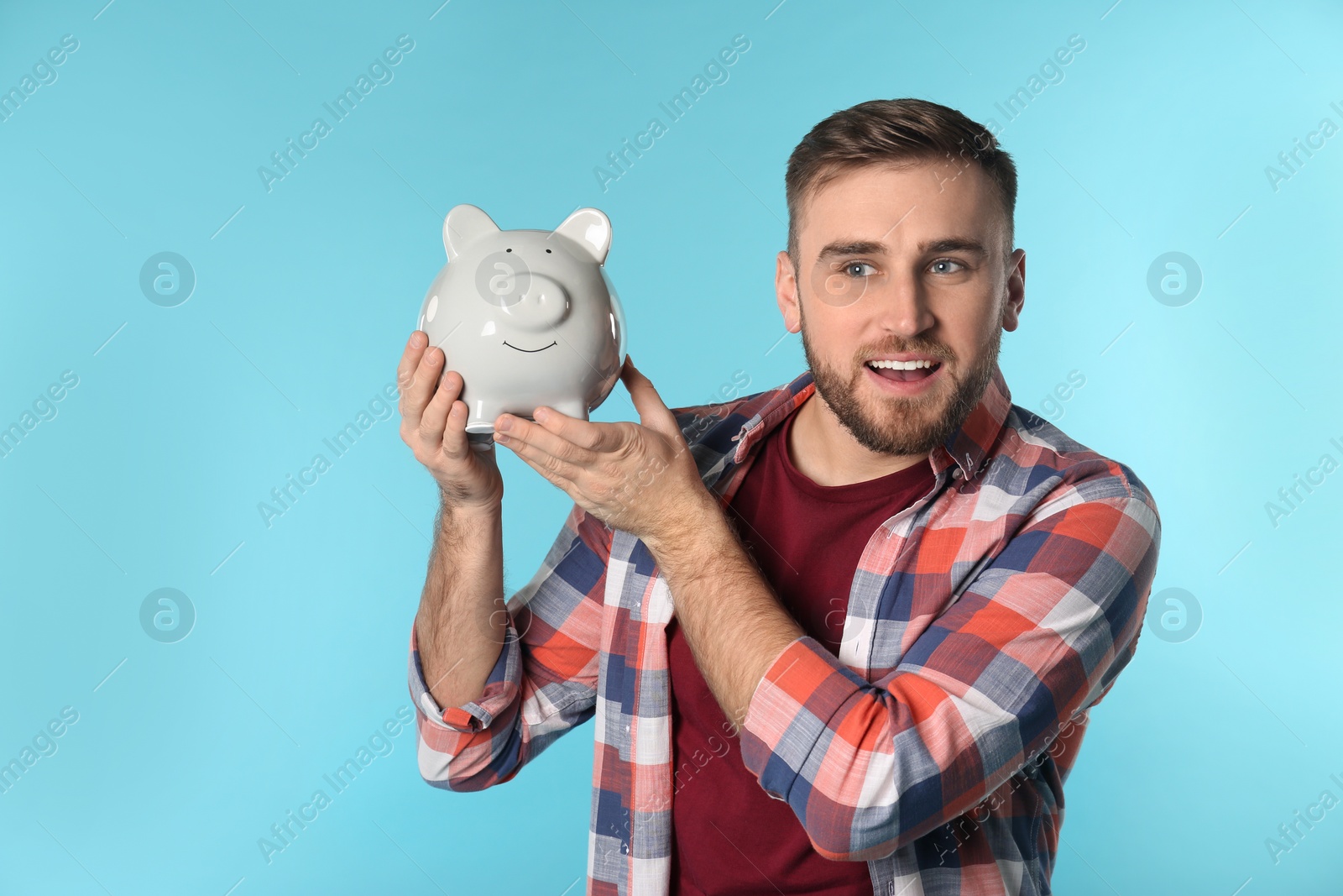 Photo of Happy young man with piggy bank and space for text on color background. Money saving