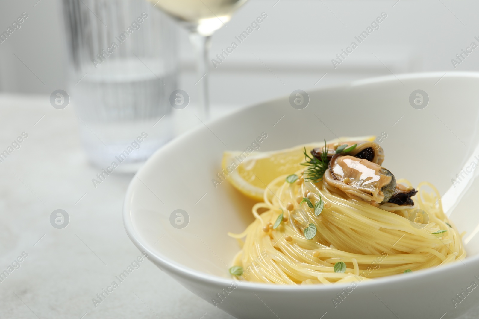 Photo of Tasty capellini with mussels and lemon served on light grey table, closeup. Exquisite presentation of pasta dish