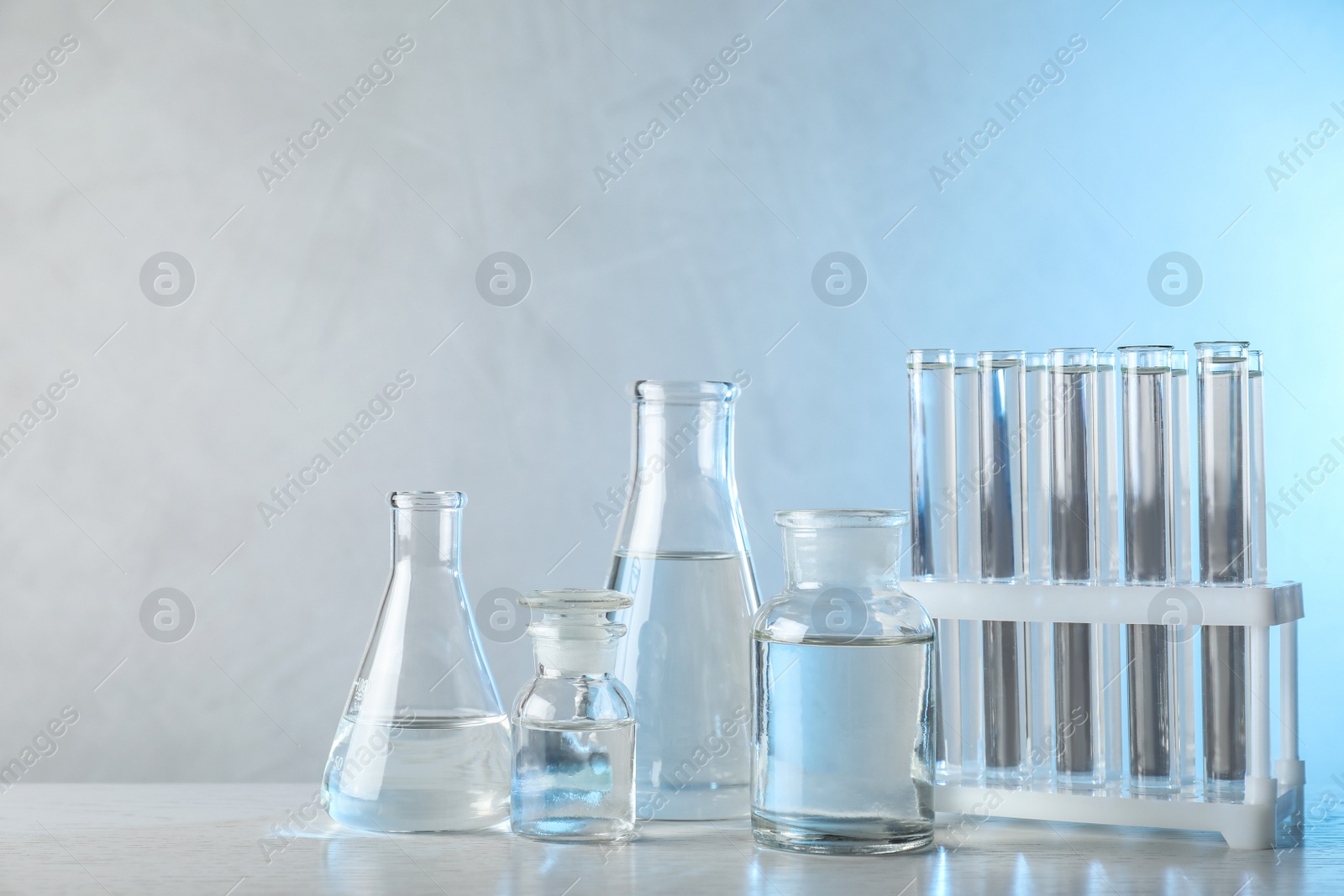 Photo of Laboratory glassware with liquid samples for analysis on table against toned blue background