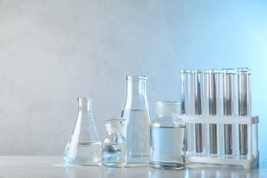 Laboratory glassware with liquid samples for analysis on table against toned blue background