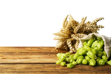 Overturned sack of hop flowers and wheat ears on wooden table against white background, space for text