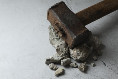 Photo of One sledgehammer and pieces of broken stones on grey background, closeup. Space for text