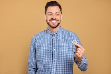 Happy man holding condom on beige background, closeup