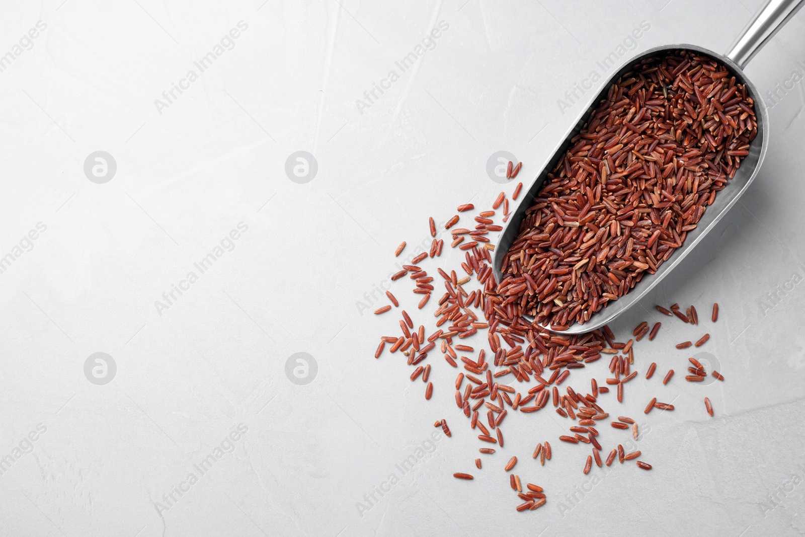 Photo of Brown rice and scoop on light grey table, top view. Space for text