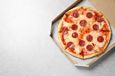 Hot delicious pepperoni pizza in cardboard box on light grey table, top view. Space for text