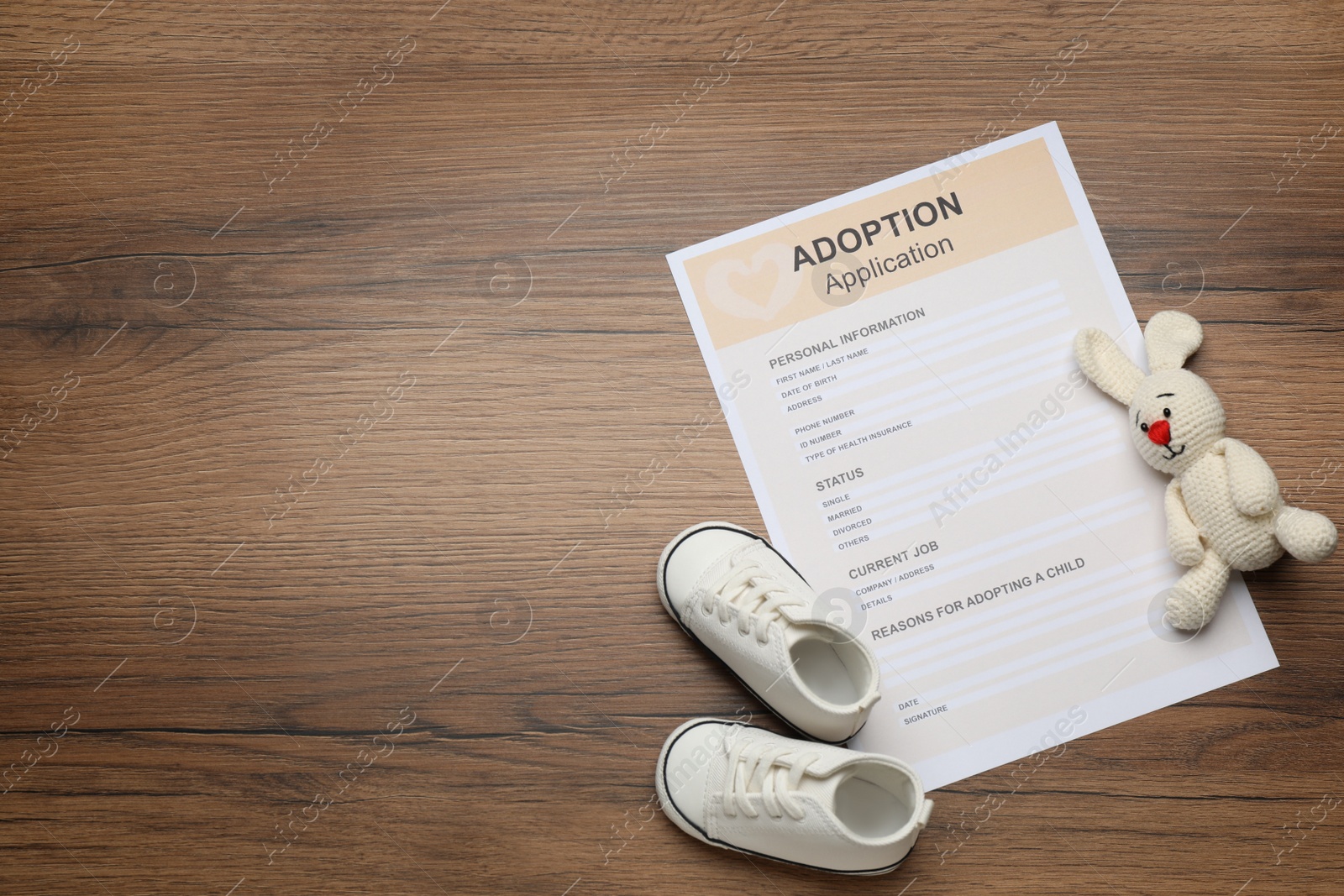 Photo of Adoption application, toy bunny and baby shoes on wooden table, flat lay. Space for text