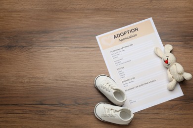 Photo of Adoption application, toy bunny and baby shoes on wooden table, flat lay. Space for text