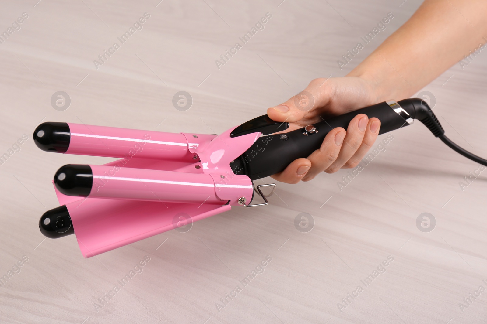 Photo of Woman holding modern triple curling iron on wooden background, closeup