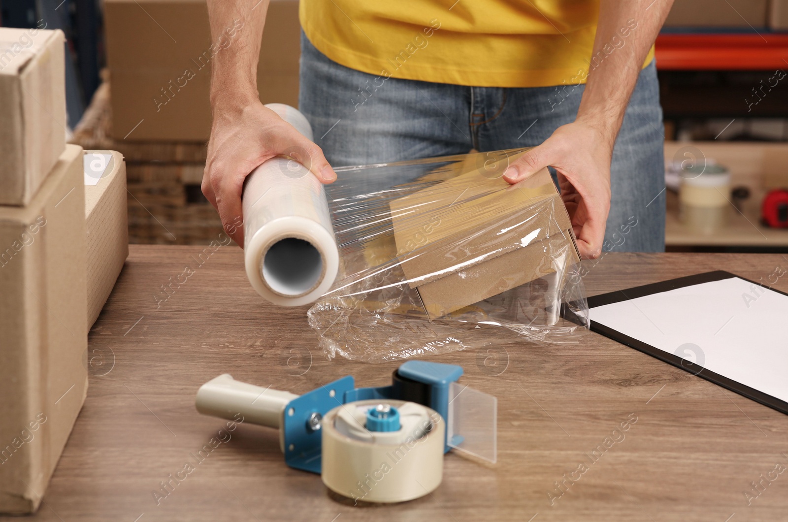 Photo of Post office worker wrapping parcel in stretch film at counter indoors, closeup