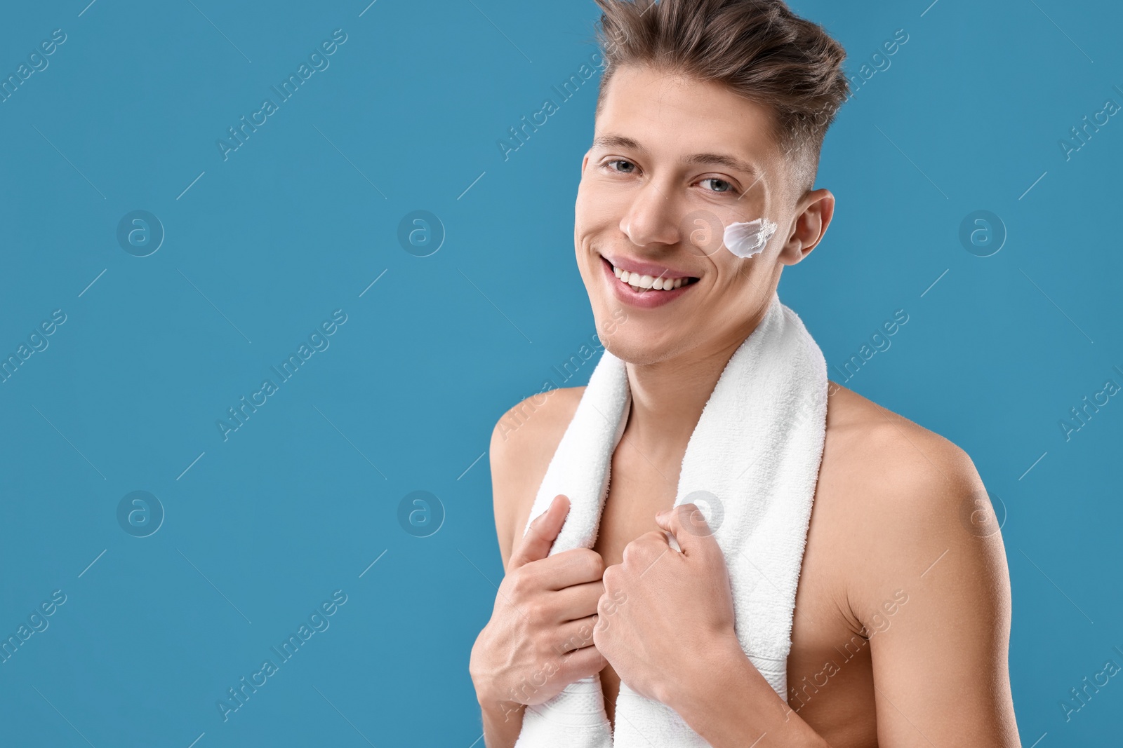 Photo of Handsome man with moisturizing cream on his face against blue background. Space for text
