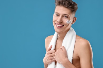 Handsome man with moisturizing cream on his face against blue background. Space for text