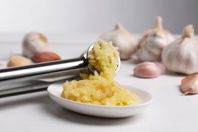 Photo of One metal press and crushed garlic on white wooden table, closeup