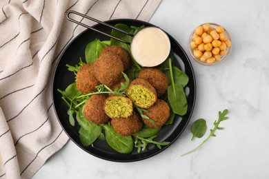 Photo of Delicious falafel balls, herbs, chickpeas and sauce on white marble table, top view