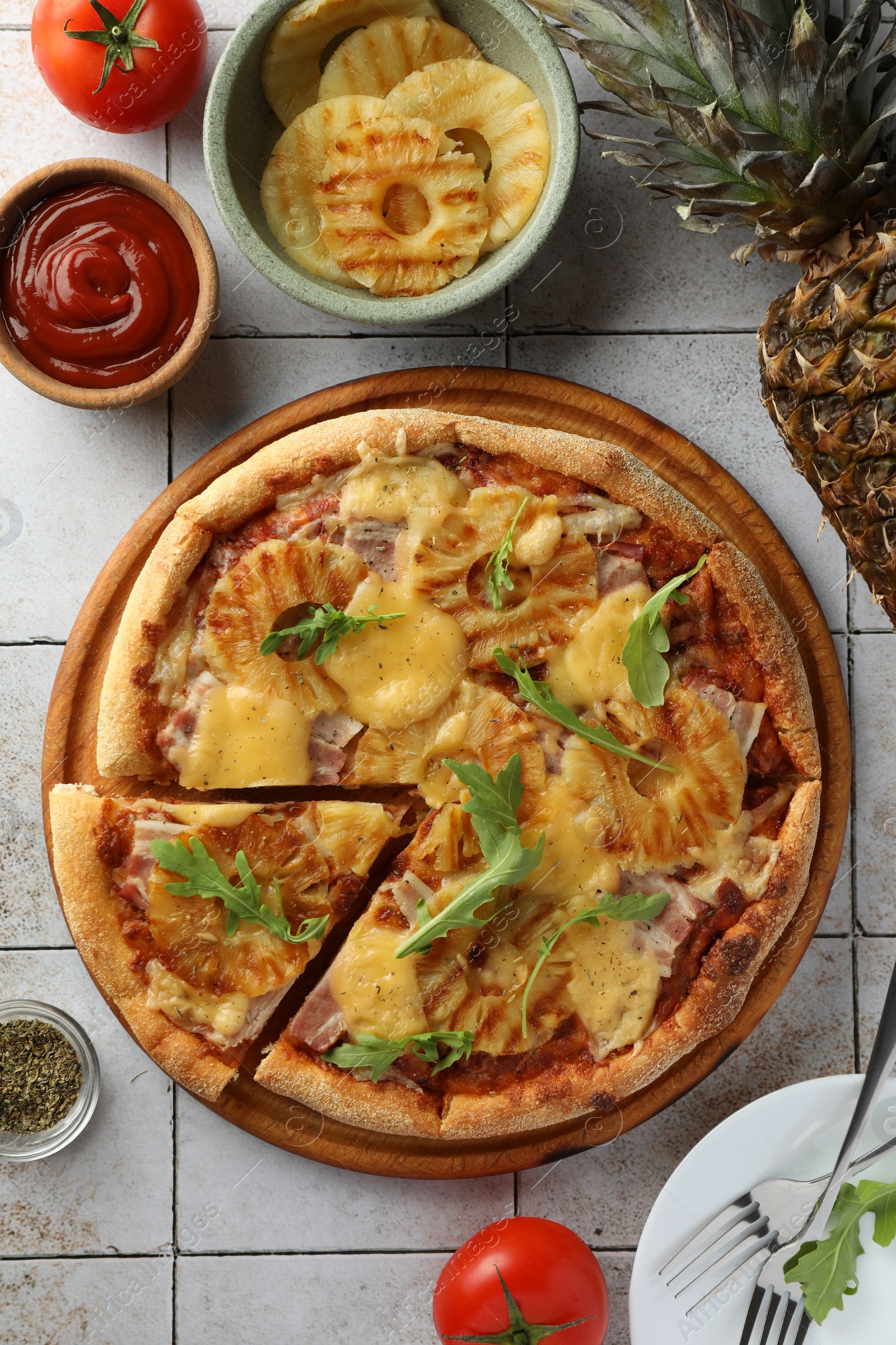 Photo of Delicious cut pineapple pizza and ingredients on light gray tiled table, flat lay