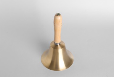 Photo of Golden school bell with wooden handle on grey background