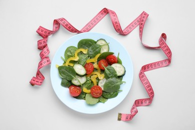 Measuring tape and salad on light background, flat lay