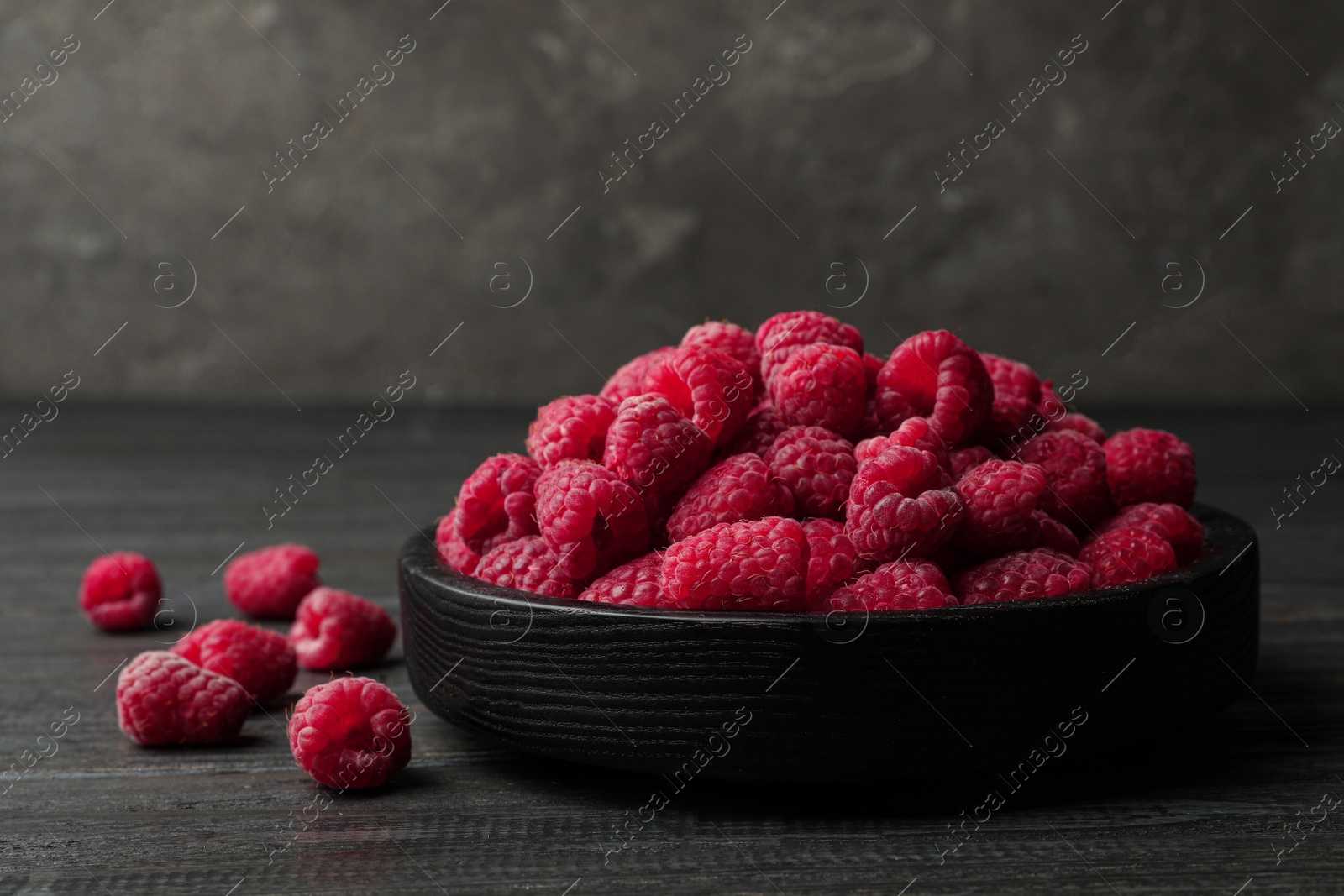 Photo of Bowl of delicious fresh ripe raspberries on dark wooden table